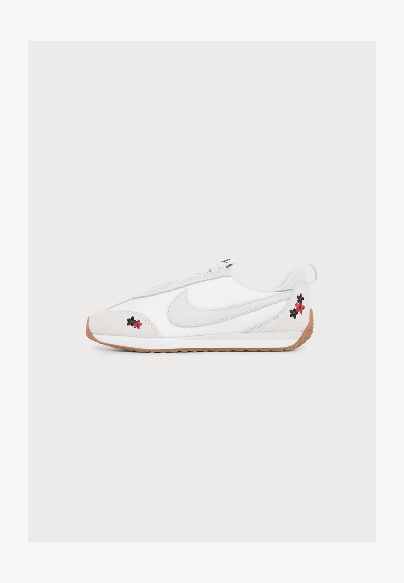 Λευκό sneaker χαμηλού προφίλ με ανοιχτό γκρι λογότυπο Nike, καουτσούκ σόλα και μικρή κόκκινη και μαύρη κεντητή ανθοδέσμη κοντά στη φτέρνα και τα δάχτυλα.