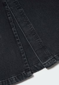 Gros plan sur un tissu en denim noir superposé avec des coutures visibles et des détails d'ourlet.