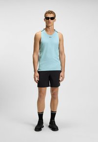 Top sportivo senza maniche di colore blu chiaro con tessuto testurizzato, pantaloni corti neri e scarpe da ginnastica nere. Presenta il logo del marchio sul petto.