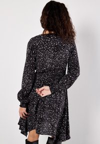 Schwarz- und grau geflecktes Kleid mit langen Ärmeln, elastischem Taillenbund, Rüschensaum und gerafften Bündchen. Weicher Stoff mit subtiler Schimmer.
