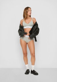 Pilkas braletė ir aukšto juosmens kelnaitės su baltu Calvin Klein elastiniu juostu, derinamos su juodu dideliu odiniu švarku ir juodomis platforminėmis loafers bateliais.