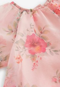 Blommig blus i mjuk rosa genomskinlig tyg, med färgglada blommönster och gröna blad. Urrigning har rynkade detaljer.