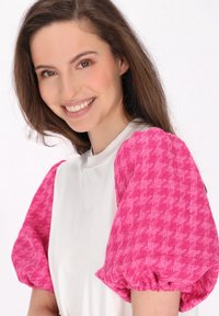 Bílý top s krátkými rukávy, který má nápadné rukávy z růžového houndstooth vzoru. Hladká textura s elastickými manžetami, které dodávají objem.