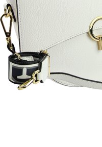 White leather handbag featuring a textured surface, gold hardware accents, and a detachable strap with a graphic black and white design.