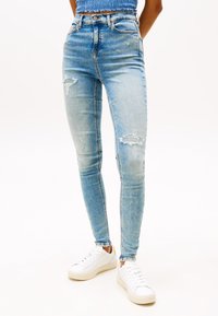 Vaaleansiniset skinny-farkut, joissa on kulutuksia, korkea vyötärö ja haalistunut pesu, yhdistettynä valkoisiin tennareihin.