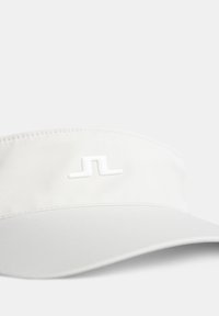 Valkoinen lippalakki, joka on valmistettu kankaasta. Siinä on kaareva lippa ja valkoinen logo edessä. Sujuva pinta ja yksinkertainen muotoilu.