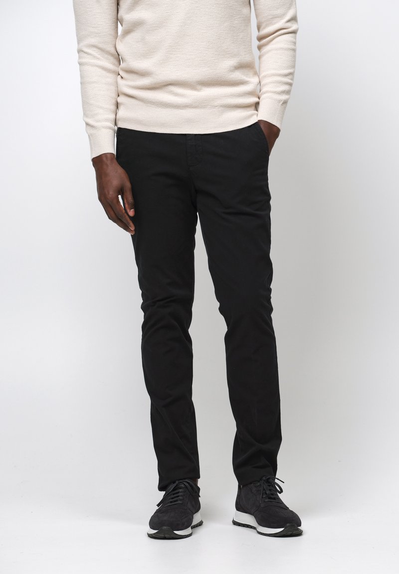 Czarne spodnie bawełniane w slim fit, z płaskim przodem i standardowymi kieszeniami, połączone z jasnobeżowym swetrem i czarnymi butami sportowymi.