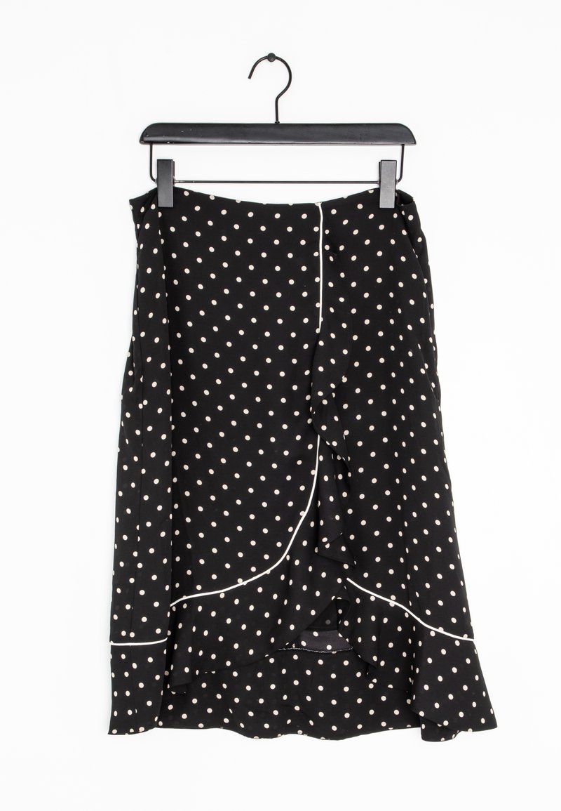 Jupe midi noire à pois blancs, bordure blanche et détail volant, suspendue sur un cintre noir sur fond blanc.