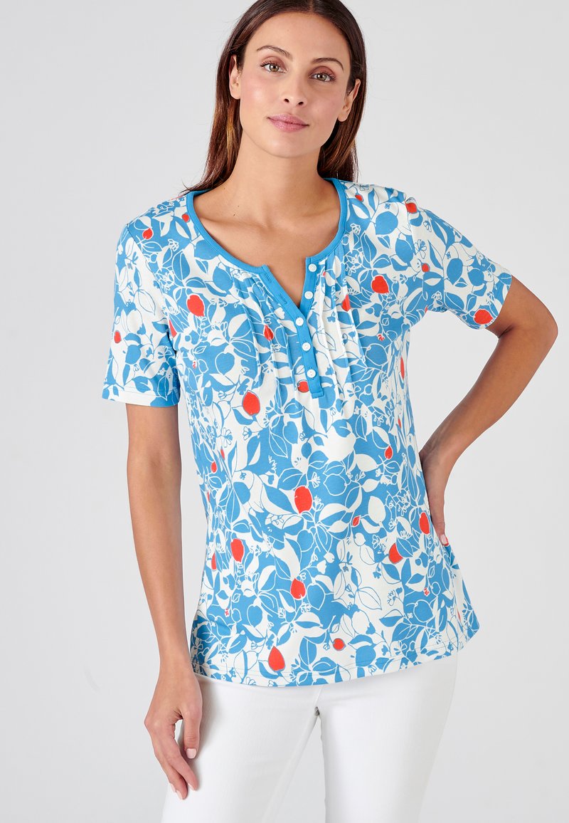 Top corto de manga azul con un patrón que presenta diseños florales en blanco y naranja, con un escote tipo henley con botones y una textura de tela suave.