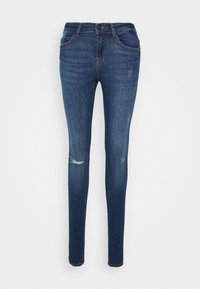 Jeans skinny em denim azul escuro, com cintura alta, ligeira descoloração e detalhes de joelhos desgastados. Design clássico de 5 bolsos com fecho de correr.
