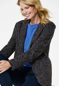 Zwarte blazer met spetterpatroon in wit en paars. Te combineren met een blauwe blouse met lange mouwen en een ronde hals.