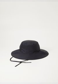 Cappello a secchiello blu navy realizzato in tessuto leggero, con una visiera larga e una cinghia per il mento regolabile. Superficie strutturata con pieghe sottili.