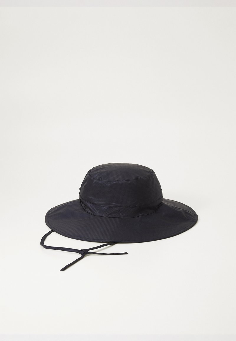 Cappello a secchiello blu navy realizzato in tessuto leggero, con una visiera larga e una cinghia per il mento regolabile. Superficie strutturata con pieghe sottili.