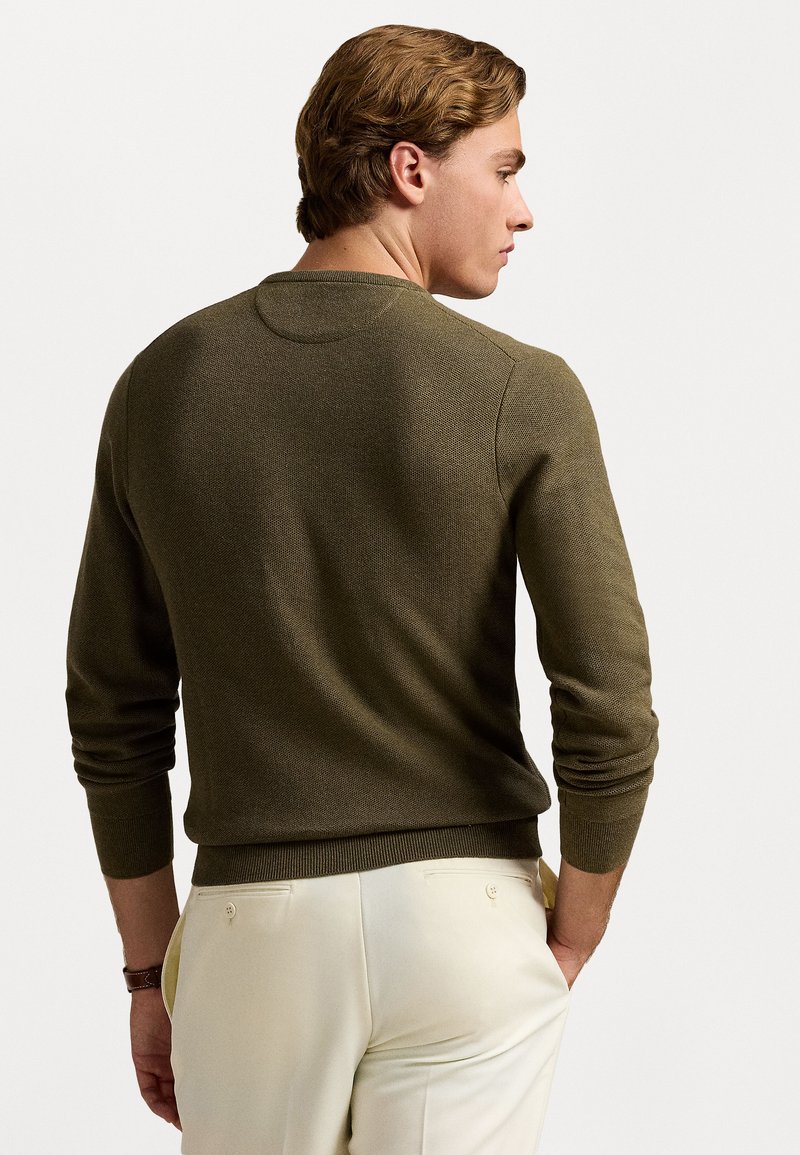Maglione a costine verde oliva con colletto rotondo, polsini e orlo a coste. Il tessuto ha una finitura testurizzata, indossato con pantaloni chiari.