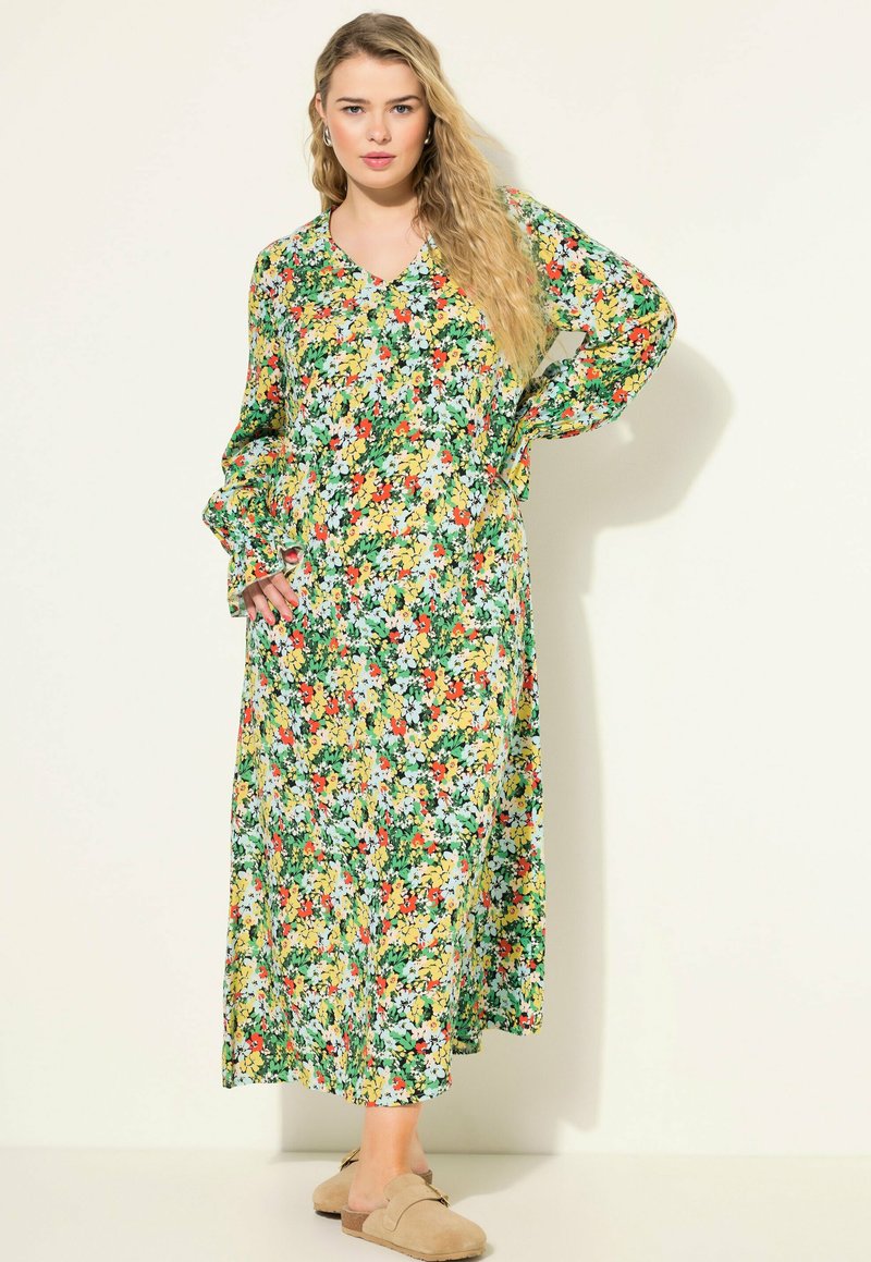 Robe maxi fleurie avec des motifs vibrants de vert, jaune, rouge et blanc. Comprend un décolleté en V et des manches longues et vaporeuses. Texture de tissu douce.