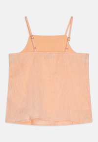 Bezruký top broskvové barvy s nastavitelnými ramínky, strukturovanou látkou a volným střihem. Má hladkou vnitřní podšívku a rovný lem.