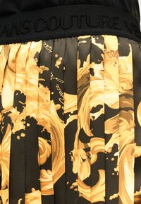 Μαύρο και χρυσό πλισέ ύφασμα με περίτεχνα μπαρόκ σχέδια και μαύρη μέση με ανάγλυφη την επιγραφή "JEANS COUTURE".