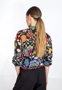 Maglione floreale colorato con sfondo nero, caratterizzato da fiori vivaci arancioni, verdi e viola, e un colletto verde. Materiale a maglia leggero.