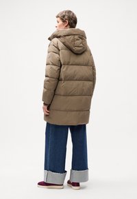 Brown puffer coat with hood, featuring horizontal stitching, a logo patch on the sleeve, and a relaxed fit. Paired with wide-leg denim pants.
