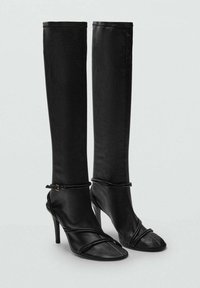Bottes à talons noires avec un design montantes jusqu'au genou. Fabriquées en cuir lisse avec un tige ajustée et un bout ouvert. Comprennent une fine sangle à la cheville.