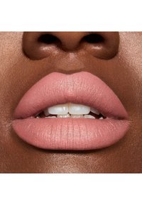 Lápiz labial mate rosa en labios llenos, mostrando una textura fina y un brillo sutil, sobre una piel oscura y suave, con dientes blancos visibles.