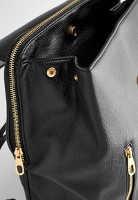 Sac à dos en cuir noir avec fermeture éclair dorée et bouton-pression légèrement ouvert, montrant un matériau texturé et une pochette intérieure.