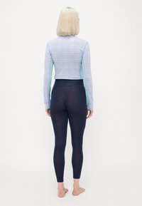 Langermet rash guard i lys blå med lilla geometrisk mønster, kombinert med tettsittende mørkeblå tights. Myk, stretchy stoff, sømløst design.