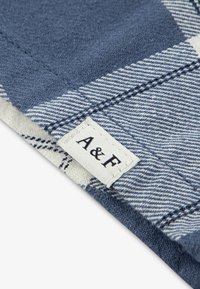 Μπλε και λευκό καρό ύφασμα με υφή. Ορατή ετικέτα με το λογότυπο "A&F", που δείχνει λευκό φόντο και μαύρα γράμματα.