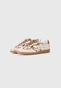 Sneakers with a white canvas upper featuring brown splatter patterns, brown laces, and a textured tan rubber sole.
