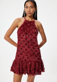 Robe halter bourgogne en tissu doux et texturé avec des sequins, un ourlet froncé et un corsage ajusté.