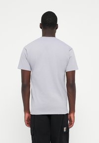Gray cotton t-shirt, short sleeves, classic crew neck design, smooth texture, worn with black cargo pants. Back view, plain fabric, no patterns.