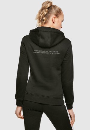 Sort hoodie med hætte, ribbede manchetter og kant. Teksten på ryggen lyder: "HVOR HVER MELODI DE SKABER SAMMEN ER EN SYMFONI AF KÆRLIGHED."