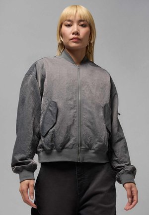 Veste bomber grise avec fermeture éclair à l'avant, poignets côtelés et deux poches avant. Tissu texturé avec une légère brillance, coupe décontractée.