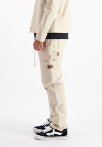 Beige cargobroeken van een textuurstof, met zijzakken en een logo-opdruk. Gecombineerd met zwart-witte sneakers.