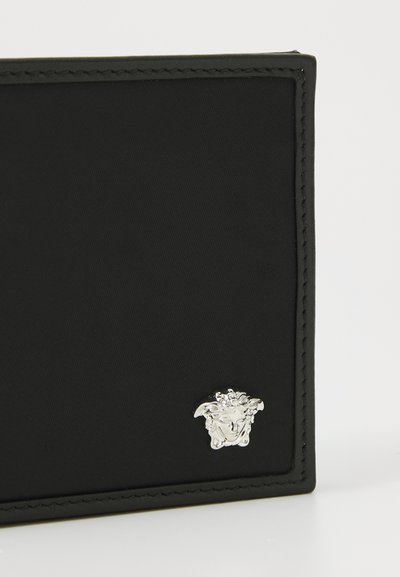 Black nylon wallet featuring a textured surface, finished with silver-tone hardware detail in the shape of a face logo, and stitched edges.