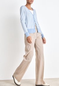 Cardigan a righe blu chiaro e bianche con scollo a V, chiusura con bottoni e polsini a costine, abbinato a pantaloni beige ampi e testurizzati.