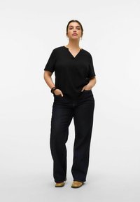 Blusa negra de manga corta con escote en V, combinada con jeans de pierna recta oscuros y zuecos beige, con una textura suave y un diseño minimalista.