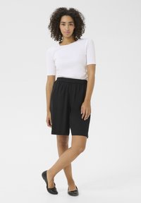 Shorts neri con vita elastica e due tasche laterali, abbinati a una maglietta bianca aderente. Il tessuto sembra leggero con una finitura liscia.