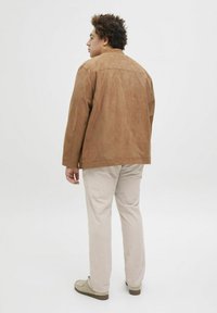 Veste en daim marron au coupe décontractée, avec des coutures minimales et des manches mi-longues. Assortie à un pantalon beige clair et des chaussures beiges.