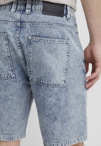 Világoskék farmer sort, elhalványodott textúrával, két hátsó zsebbel és egy fekete bőr címkével a derékrészen.