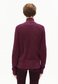 Lila gerippter Pullover mit hohem Kragen und langen Ärmeln, kombiniert mit dunkel gemusterten Leggings im Zebra-Streifen-Design.