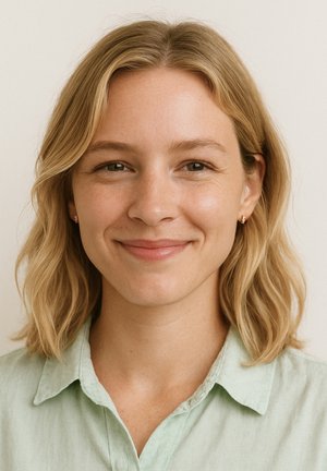 Ritratto di una persona con capelli biondi ondulati fino alle spalle, che indossa una camicia leggera verde chiaro, sorridendo su uno sfondo neutro.