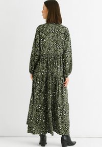 Long green dress with a black and white leopard print, gathered waist, long sleeves, and flowing fabric. Worn with black ankle boots.
