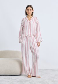 Białe piżamy w paski z czerwonymi pionowymi liniami, składające się z koszuli na guziki i spodni z troczkami. Miękka tkanina o luźnym fasonie.