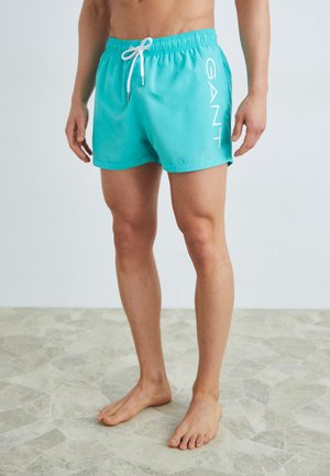 Bañador azul claro con una cinturilla elástica y cordones blancos, y un gran logo blanco en el lado izquierdo. Textura suave.