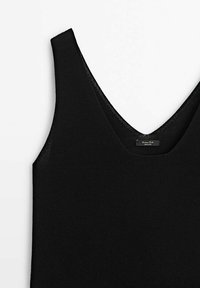 Haut en maille noir sans manches avec de larges bretelles et un décolleté en V, posé à plat sur une surface blanche.
