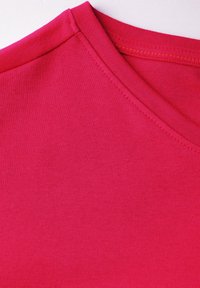 Heldere roze T-shirt met een V-hals ontwerp, gemaakt van soepel, lichtgewicht stof met platte naden en een zachte textuur.