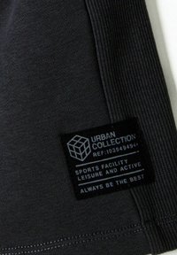 Zwarte sporttop met een gematteerd ribbelontwerp, voorzien van een label met de tekst "Urban Collection" met wasinstructies en een logo.
