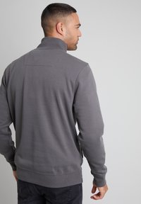Grau Sweatshirt mit hohem Kragen, langen Ärmeln und gerippten Bündchen. Besitzt eine glatte Textur und ein dezentes Nahtdetail auf der Rückseite.