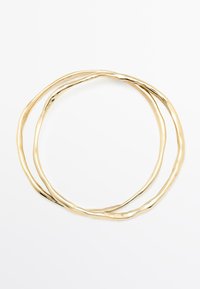 Bracciale dorato intrecciato con due anelli intrecciati, caratterizzato da una superficie liscia e lucida e una forma organica irregolare, che riflette la luce.